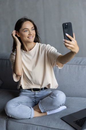 Portrait of a beautiful brunette taking a selfie with her smart phone at homeの写真素材