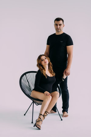 A man in love hugs a beautiful pregnant woman with a big belly sitting on a wicker wooden chair on a...