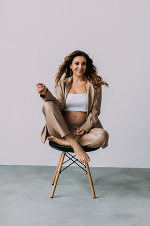 Attractive smiling young pregnant woman sitting on a chair isolated over white background, showing peace gestureの写真素材