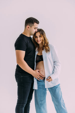 Happy Couple Expecting Baby. Beautiful Young Pregnant Woman and Her Husband Sitting Together and Caressing Her Pregnant Belly. Isolated on white background. mom and dadの写真素材