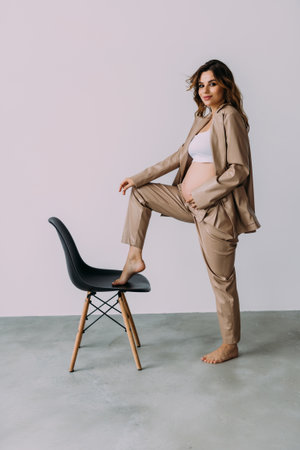 Pregnant woman sitting on chair, wearing casual comfortable clothes isolated in studio. concept of maternityの写真素材