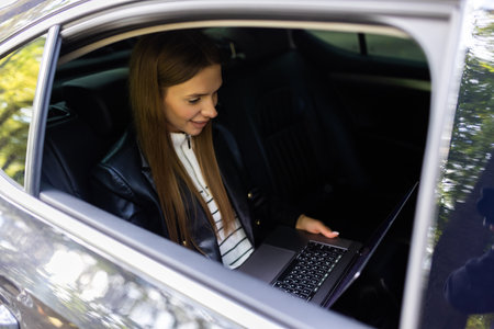 Beautiful young business woman is using laptop in the car to workの写真素材