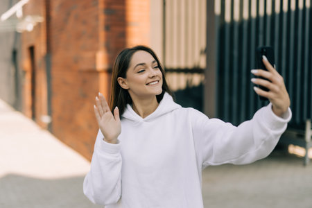 Young smiling woman in coat taling selfie on mobile phone in evening city streetの写真素材