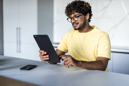 Indian Man Using Digital Tablet Whilst Eating Breakfastの写真素材