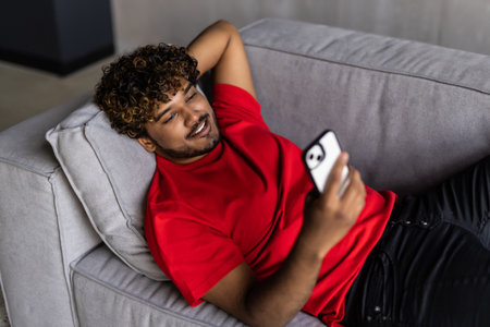 Relaxed asian man using a smart phone lying on couch in the living room at homeの写真素材
