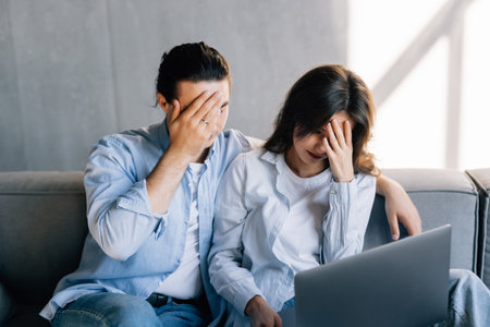 Confused upset millennial married couple sit on couch read financial papers invoices troubled with too high expenses utility costs. Worried young spouses deal with debt bankruptcy of family businessの写真素材