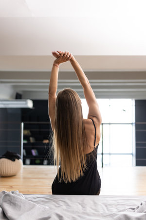 Rear view of woman stretching in bed after waking up in the morning with sunlightの写真素材
