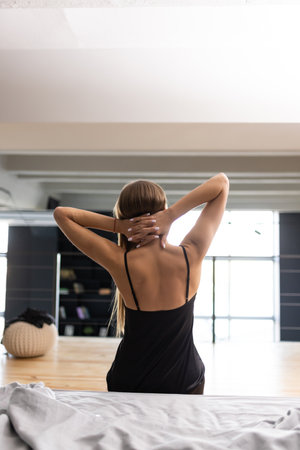 Rear view of woman stretching in bed after waking up in the morning with sunlightの写真素材