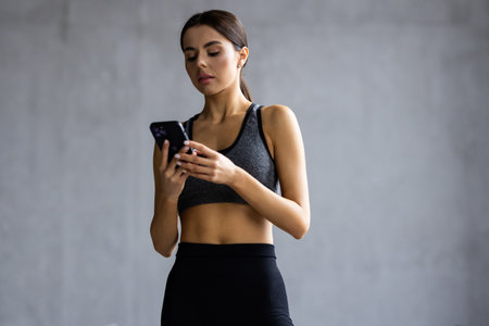 Attractive healthy young woman with a fitness mat using mobile phone at the yoga studio
