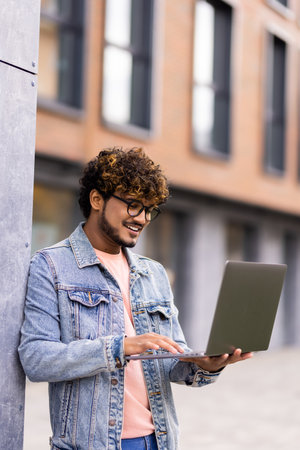 Handsome young indian businessman holding his laptop while standing on the streetの写真素材