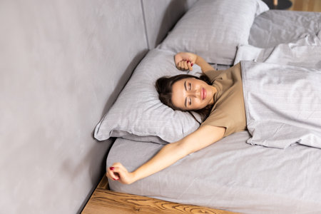 Young beautiful smiling girl stretching in her bed with white bedclothes early in the morning