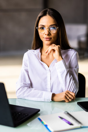 Concentrated young beautiful businesswoman working on laptop in bright modern officeの写真素材