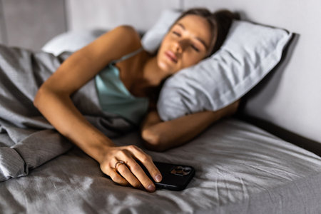 woman sleeping in bed being woken by mobile phoneの写真素材