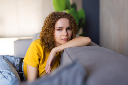 Happy young woman sitting on sofa at home and looking at camera. Portrait of beautiful girl smiling and relaxing during autumn.の写真素材