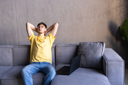 Portrait of a casual tired man resting sitting on a couch at homeの写真素材