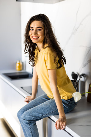 Young woman looking at camera while sitting on the kitchen counterの写真素材