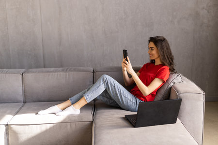 Excited woman watching media content on line in a mobile phone sitting on a couch in the living roomの写真素材