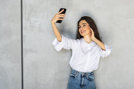 Young business woman studio isolated on gray wall taking selfie photos looking camera smiling joyfulの写真素材