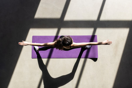 Health practice concept. Top view portrait of young flexible female doing seated forward bend yoga exercise on mat with laptop. Copy space on leftの写真素材