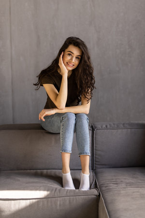 Smiling pretty woman in sweater using tablet computer while sitting on a windowsill at homeの写真素材