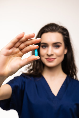 Pointing at pills. Portrait of young woman, doctor, therapeutic or medical advisor wearing face mask and blue uniform on white background. Concept of healthcare and medicineの写真素材