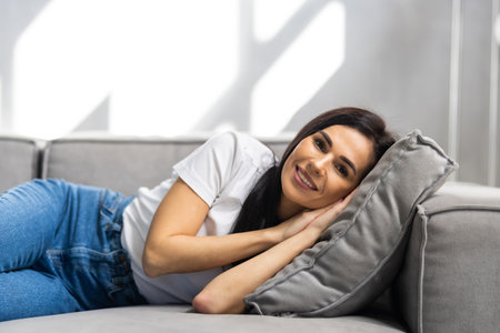Tired young woman lying on cozy couch take nap daydreaming in living room, peaceful girl relax on comfortable sofa with eyes closed sleeping resting at home, female feel fatigue fall asleepの写真素材