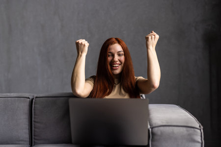 Happy young woman with credit card and laptop sitting on sofa at homeの写真素材