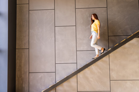 Young woman going down the stairs in modern house holding box with clothes.の写真素材