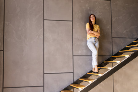 Confident young woman stand the staircase in the kitchen at homeの写真素材