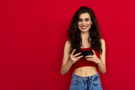 Photo of satisfied woman in black clothing looking on camera while using cell phone with joy over...