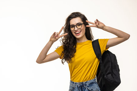 Lovely charismatic caucasian redhead girl with backpack, headphones over neck, showing peace sign and smiling delighted and joyful camera, standing white background, heading part-time jobの写真素材