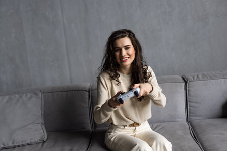 Passionate gamer. Excited woman spend leisure time for playing console videogame. Overjoyed female sit on cozy sofa at home hold gamepad enjoy favorite computer gameの写真素材