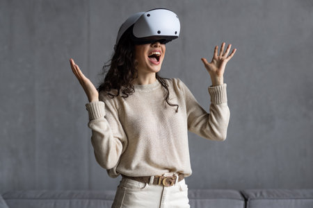 Beautiful young girl in virtual reality headset. augmented reality. Happy woman holds 3D vr glasses indoors, wide smiles opens mouth in happy expression. Woman plays using VR goggles at home office.の写真素材