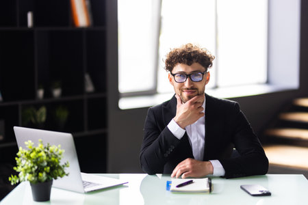 Happy young man, wearing glasses and smiling, as he works on his laptop to get all his business done early in the morning with his cup of coffeeの写真素材