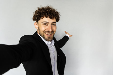 Image of successful man 30s in business suit gesturing hand aside while taking selfie photo isolated over gray backgroundの写真素材