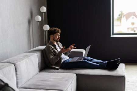 Young man is browsing at his laptop and calling with customer on the sofa at home, Business successの写真素材