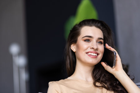 Happy woman talking on mobile phone sitting on comfortable couch at home, copy space