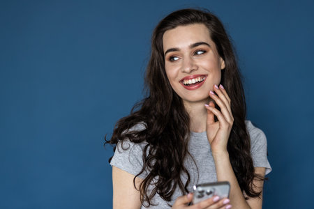 Young woman hold in hand use phone isolated on blue cyan background. people lifestyle conceptの写真素材