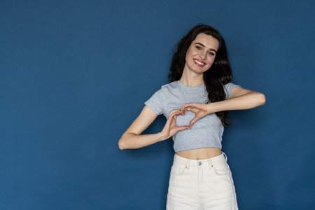 Young woman over blue isolated background smiling in love doing heart symbol shape with hands. romantic concept.の写真素材
