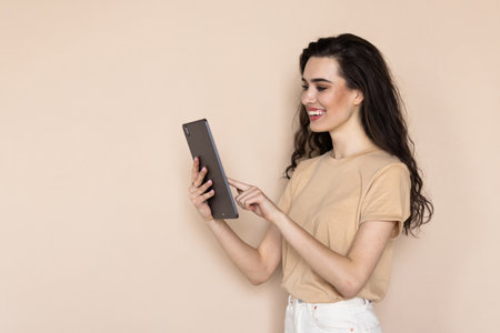 A young girl with a tablet in her hands on a beige background. Beautiful girl with a tablet in her handsの写真素材