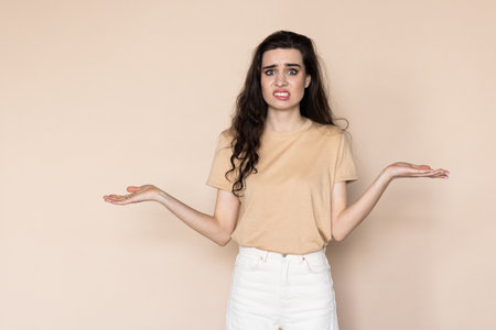 Young woman isolated on beige background makes scale with armsの写真素材