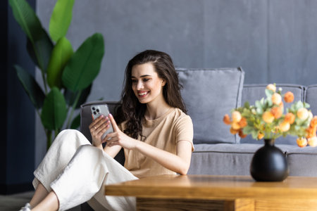 Young woman using mobile phone while sitting a couch at homeの写真素材