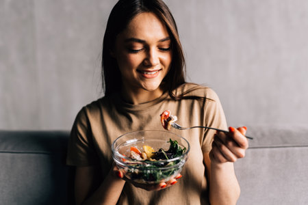Happy woman relaxing on the sofa eating salad in her living roomの写真素材