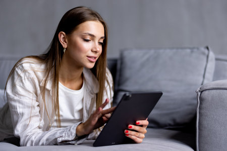 Young woman sitting on couch at home with tablet computerの写真素材