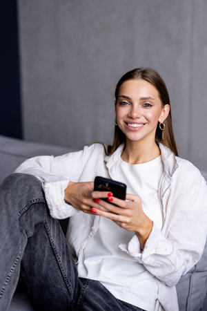 Happy young asian woman using mobile phone while sitting a couch at home with laptop computer