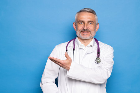 handsome doctor man wearing coat and stethoscope over isolated blue backgroundの写真素材