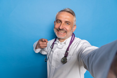 Telemedicine and Virtual Consultations. Handsome middle aged doctor using digital tablet to conduct remote appointments, diagnose patients, provide medical advice, blue background, copy spaceの写真素材