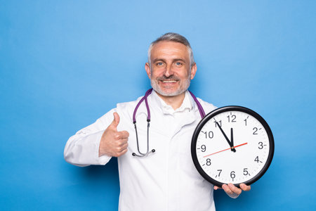 Smiling male doctor in lab coat with arms crossed against blue background.の写真素材