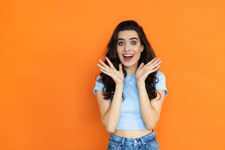 Frightened person showing shocked facial expression, standing over orange background. Anxious woman feeling scared and terrified while looking at camera. Panicked adult with hands upの写真素材