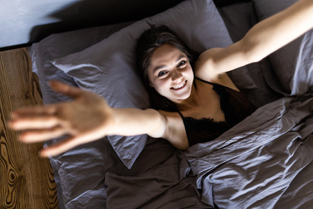 Happy girl waking up stretching arms on the bed in the morningの写真素材